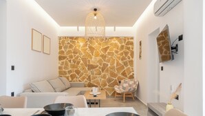 Una sala moderna con pared de piedra, un sofá, una mesa de comedor con cuencos y un televisor montado en la pared.