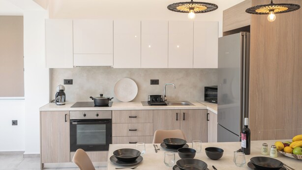 Una cocina moderna con armarios de madera clara, un refrigerador de acero inoxidable y un comedor con una mesa dispuesta para cuatro.
