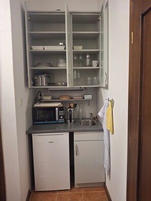 Eine kompakte Küche mit integriertem Mikrowellenherd, einem kleinen Kühlschrank und einem Spülbecken.