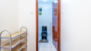 Ein schmaler Flur führt zu einem Badezimmer mit Toilette, Waschbecken und Dusche. Links befindet sich ein Metallregal mit einer Holzablage.