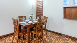 Ein Essbereich mit einem Holztisch, gedeckt für vier Personen, umgeben von passenden Stühlen. Auf dem Tisch steht eine Zierpflanze und zur Rechten eine Schranke mit Glastüren.