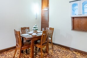 Ein Essbereich mit einem Holztisch, gedeckt für vier Personen, umgeben von passenden Stühlen. Auf dem Tisch steht eine Zierpflanze und zur Rechten eine Schranke mit Glastüren.