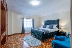 A bedroom with a tufted headboard bed, a wooden wardrobe, a blue sofa, and a patterned floor. - Fabulous 2-bedroom penthouse apartment in vibrant Kileleshwa for your stay (Nairobi)