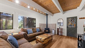 Un salon chaleureux avec un plafond en bois, une cheminée en briques, un canapé agrémenté de coussins à motifs et une table basse en bois.