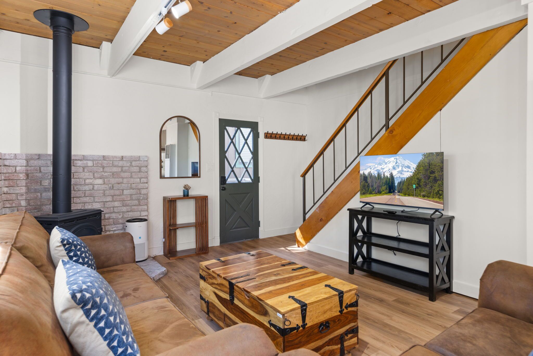A modern living room with a wooden staircase, a fireplace, a large TV, and a cozy sofa.