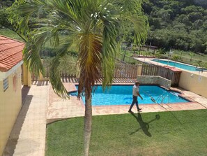 A swimming pool with a palm tree in the foreground, a wooden fence, and a building with a tiled roof in the background. - Spacious, Breezy 2 bdrm Condo! Great Location between Jobos Beach & Shacks Beach (Isabela)