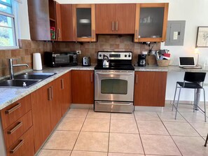A modern kitchen with wooden cabinets, stainless steel appliances, a double sink, and a bar stool. - Spacious, Breezy 2 bdrm Condo! Great Location between Jobos Beach & Shacks Beach (Isabela)