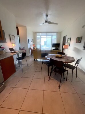 A spacious living area with a dining table, chairs, a sofa, and a kitchen area with a counter and chairs. - Spacious, Breezy 2 bdrm Condo! Great Location between Jobos Beach & Shacks Beach (Isabela)
