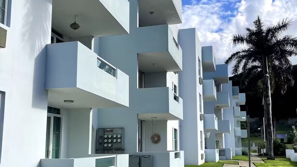 Un edificio moderno con varios balcones y un césped cuidado.