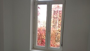 A bedroom with a single bed, a nightstand, a lamp, and a window with a view of autumn foliage. - Lille Centre Lille Europe station (Lille)
