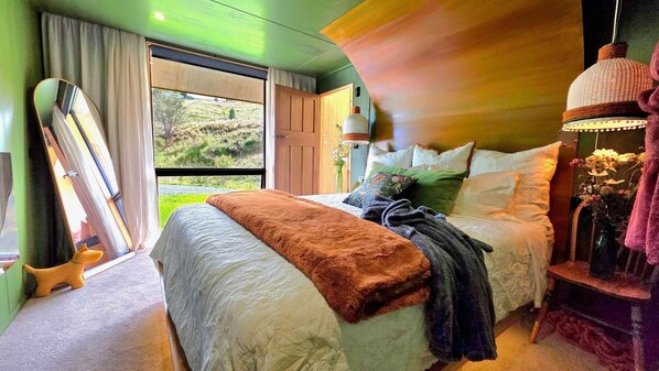 A bedroom with a large bed, a window with curtains, a wooden headboard, and a hanging lamp.