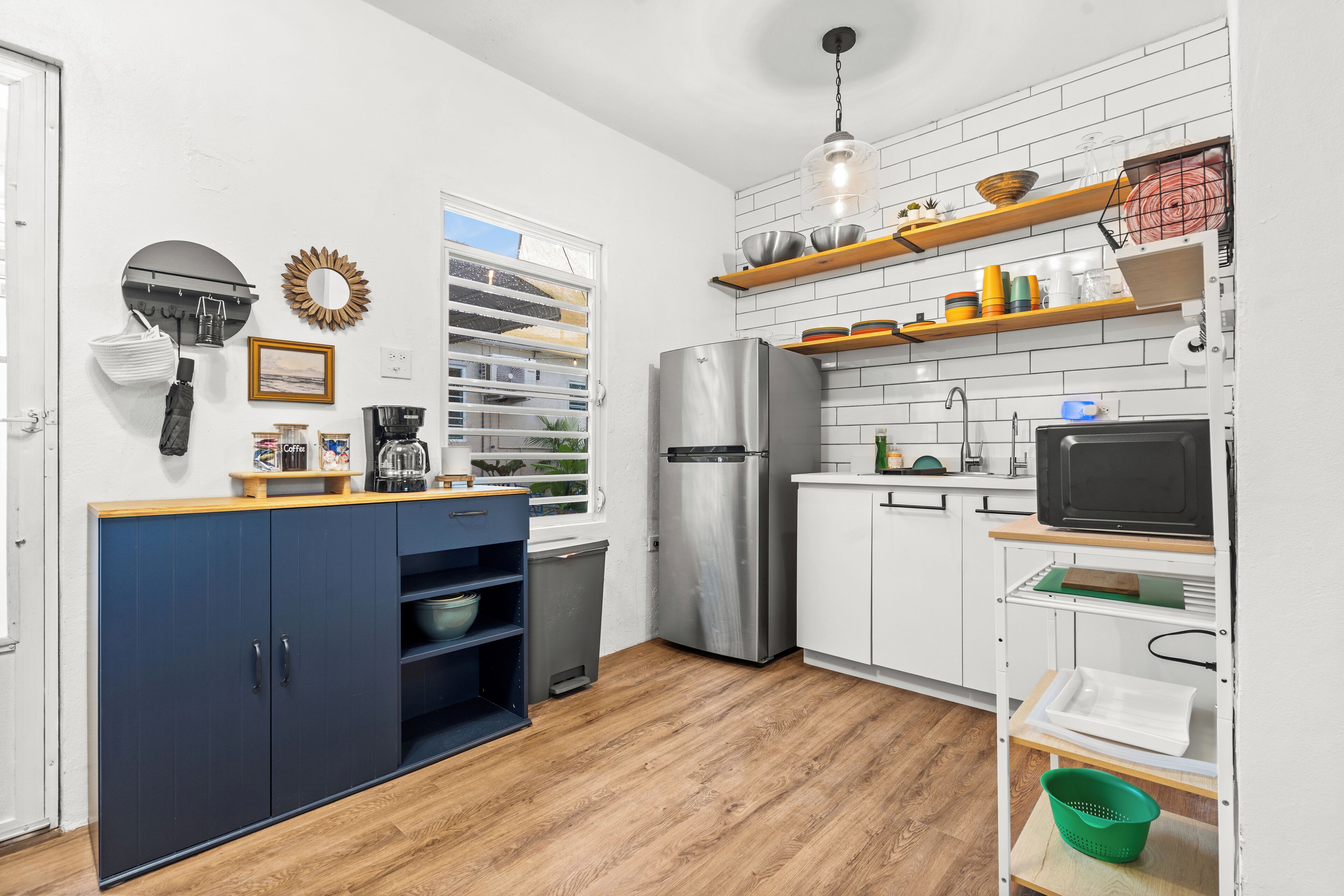 Una cocina moderna con armarios blancos, un refrigerador de acero inoxidable, estantes de madera y un microondas.
