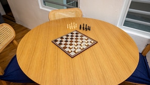 A round wooden table with a chessboard in the center, surrounded by four chairs with blue cushions. - Unique 2-Home Family Getaway Near Beaches Airport Restaurants.  Ideal for Groups (Arenales)