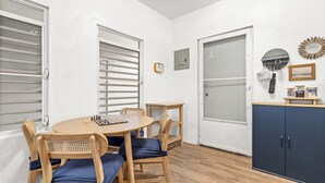 Una habitación con una mesa de comedor de madera, sillas, una pequeña mesita auxiliar de madera, un armario y una puerta con panel de vidrio esmerilado.