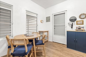 Una habitación con una mesa de comedor de madera, sillas, una pequeña mesita auxiliar de madera, un armario y una puerta con panel de vidrio esmerilado.