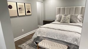 Une chambre à coucher moderne avec un grand lit, un banc et des œuvres d’art accrochées au mur.