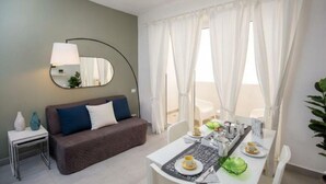 Ein modernes Zimmer mit einer Couch, einem Esstisch gedeckt mit Tellern und Tassen, einem Spiegel und transparenten Vorhängen.