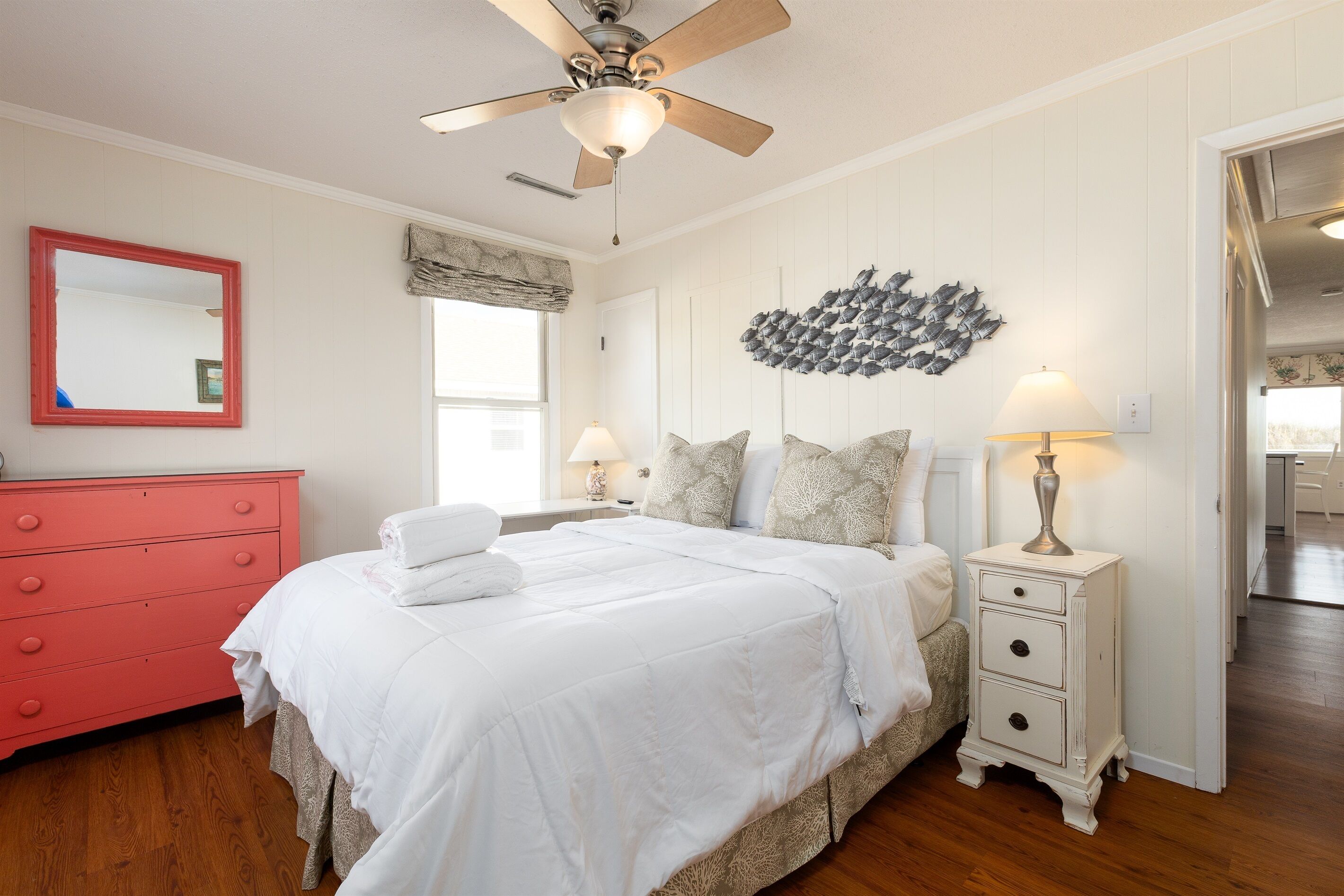 A bedroom with a bed, a ceiling fan, a dresser, a nightstand, and a wall decoration.