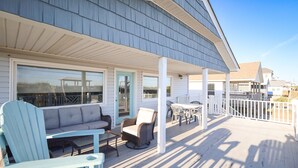 A covered outdoor deck with seating, including a sofa and chairs, and a table. - Sea Salt and Sunshine: Family & Pet Friendly (Surf City)