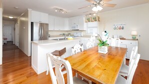 A modern kitchen with white cabinetry, a wooden dining table, and a ceiling fan. - Sea Salt and Sunshine: Family & Pet Friendly (Surf City)