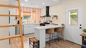 A modern kitchen with white cabinetry, a central island, two bar stools, and a wooden ladder. - Ocean Isle Retreat (Ocean Isle Beach)