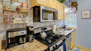 Una cocina con un refrigerador de acero inoxidable, microondas, estufa y cafetera. Hay armarios de madera, una ventana con plantas y un salpicadero con diseño.