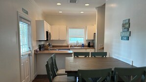 Een moderne keuken met witte kasten, een houten eettafel en groene stoelen.