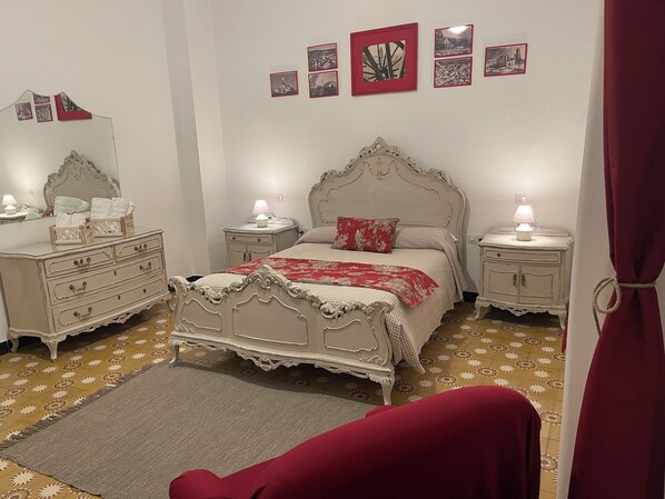 Un dormitorio con cama, mesitas de noche, cómoda, espejo y cuadros en la pared.