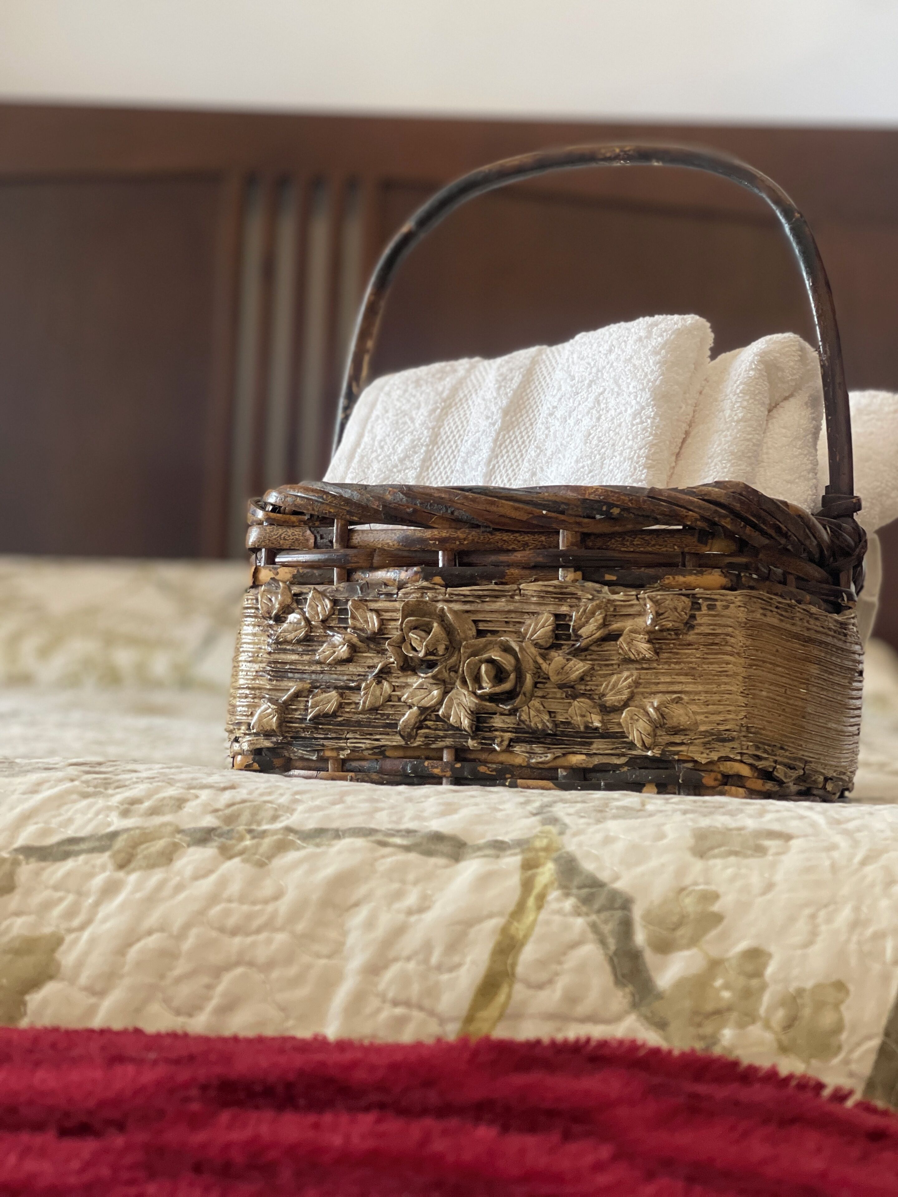 A wicker basket with a handle on a bed with a patterned bedspread.