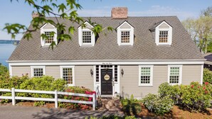 A two-story house with a front porch, a black door, and a small garden with a white fence. - The Folly PLUS, University Place View Home with Pool, Perfect  for Celebrations. (University Place)
