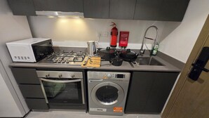 Une cuisine compacte équipée d’un four à micro-ondes, d’une cuisinière à gaz, d’un évier et d’un lave-linge.