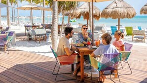 A wooden deck with a table and chairs, palm trees, and beach umbrellas. - Cancun Luxury Beachfront Resort Dec 20-Jan3 All Inclusive for 4 (Cancun)