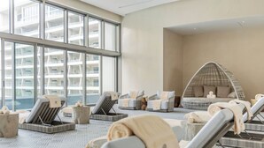 A modern indoor relaxation area with lounge chairs, a hanging chair, and a view of a high-rise building. - Cancun Luxury Beachfront Resort Dec 20-Jan3 All Inclusive for 4 (Cancun)
