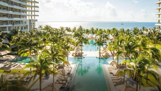 A resort with a central swimming pool surrounded by palm trees and lounge chairs, overlooking the ocean. - Cancun Luxury Beachfront Resort Dec 20-Jan3 All Inclusive for 4 (Cancun)