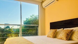 A hotel room with a large window, a bed with a beige bedspread, and two patterned pillows. - Hotel Payara (Puerto Gaitán)