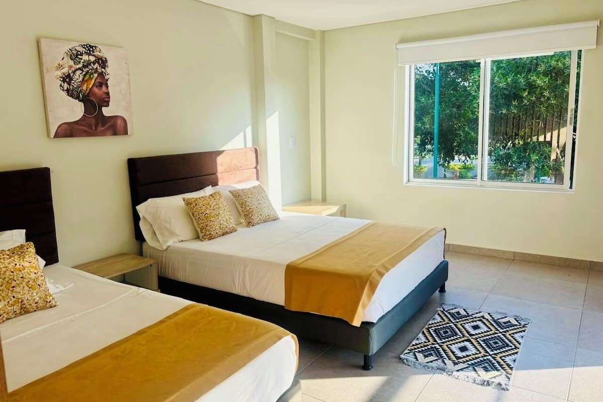 Una habitación de hotel con dos camas, un ventanal con vistas a zonas verdes y un cuadro en la pared.