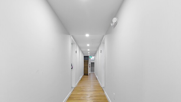 Ein schmaler, gut beleuchteter Flur mit weißen Wänden und Holzboden, der zu einer Treppe führt.