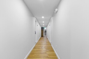 A narrow, well-lit hallway with white walls and wooden flooring, leading to a staircase. - down town location ,brand new units #4 (Gatineau)