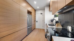 Una cucina moderna con mobili in legno, elettrodomestici in acciaio inossidabile e una parete di fondo rivestita di piastrelle nere.