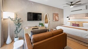 Una camera d'albergo moderna con un letto grande, una TV a schermo piatto, una scrivania, un divano e una ventola a soffitto.