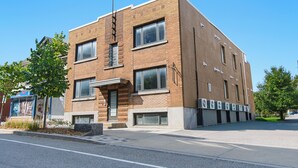 Un edificio de varios pisos de ladrillo con grandes ventanales, una entrada visible y una acera en la parte delantera.