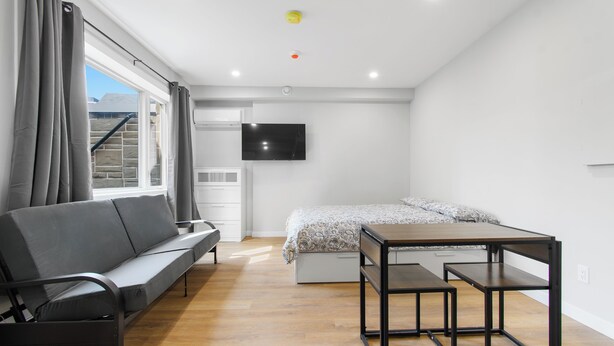 Un dormitorio moderno con sofá, cama, televisor y una mesa de madera.