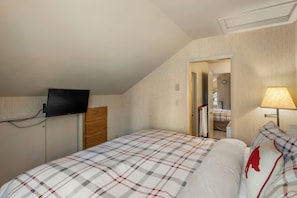 Ein Schlafzimmer mit einem Bett, einem an der Wand montierten Fernseher, einer Nachttischlampe und einer Tür zu einem Badezimmer.