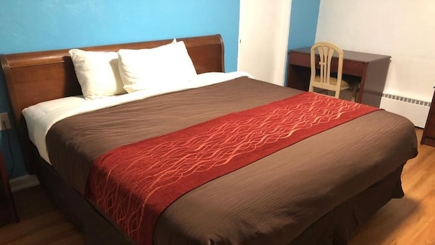 Ein Bett mit einer braunen und roten Tagesdecke, einem Holz-Kopfteil und weißen Kissen.