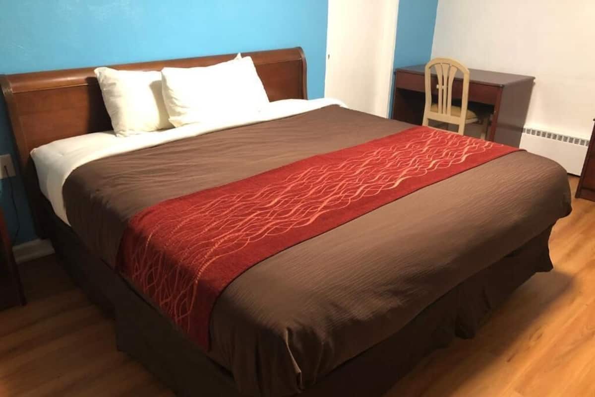 A bed with a brown and red bedspread, a wooden headboard, and white pillows.