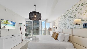 Ein modernes Schlafzimmer mit einem großen Bett, einem Fernseher, einem Schreibtisch und Blick auf die Stadt.