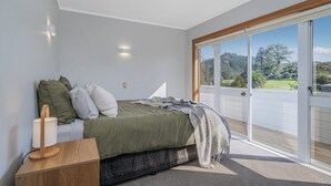 A bedroom with a bed, bedside table, and a view through a sliding glass door to the outdoors.