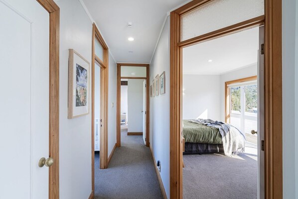 A hallway leading to a bedroom with a bed, framed pictures on the walls, and a view of the outdoors through a door.