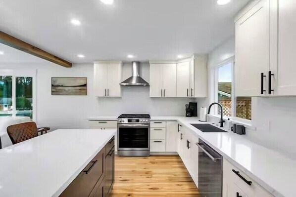 Una cocina moderna con armarios blancos, una campana extractora de acero inoxidable y una isla grande con un fregadero.