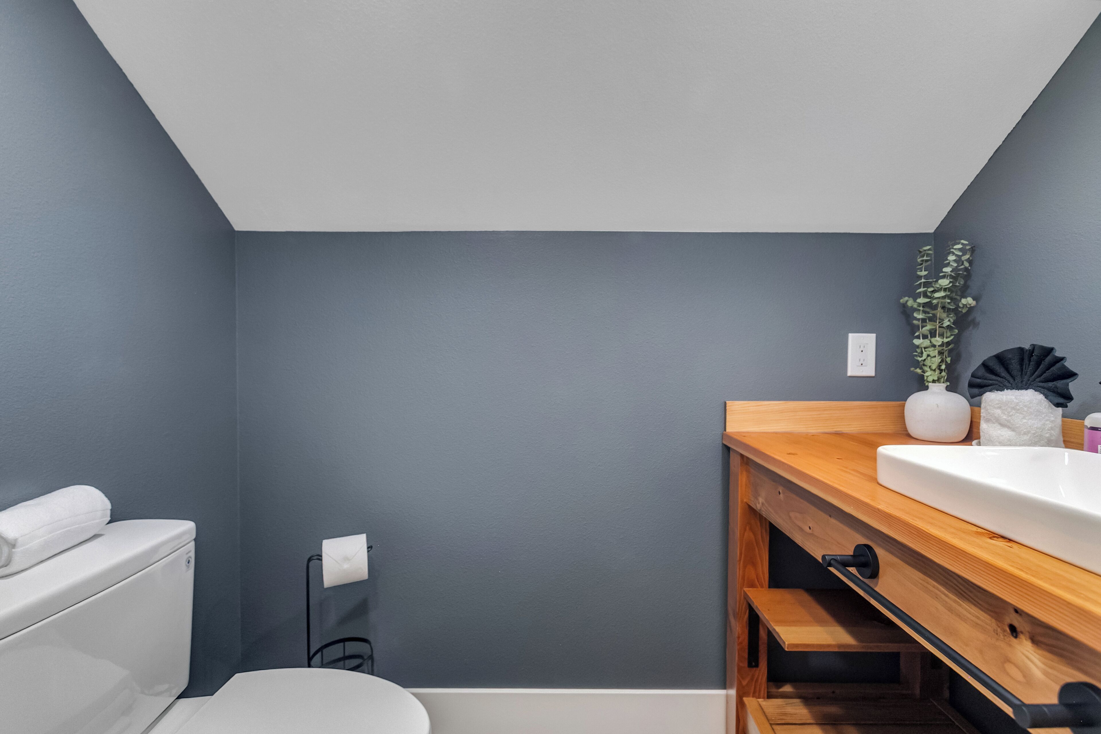 A bathroom with a white toilet, a wooden vanity with a sink, and a dark grey wall.